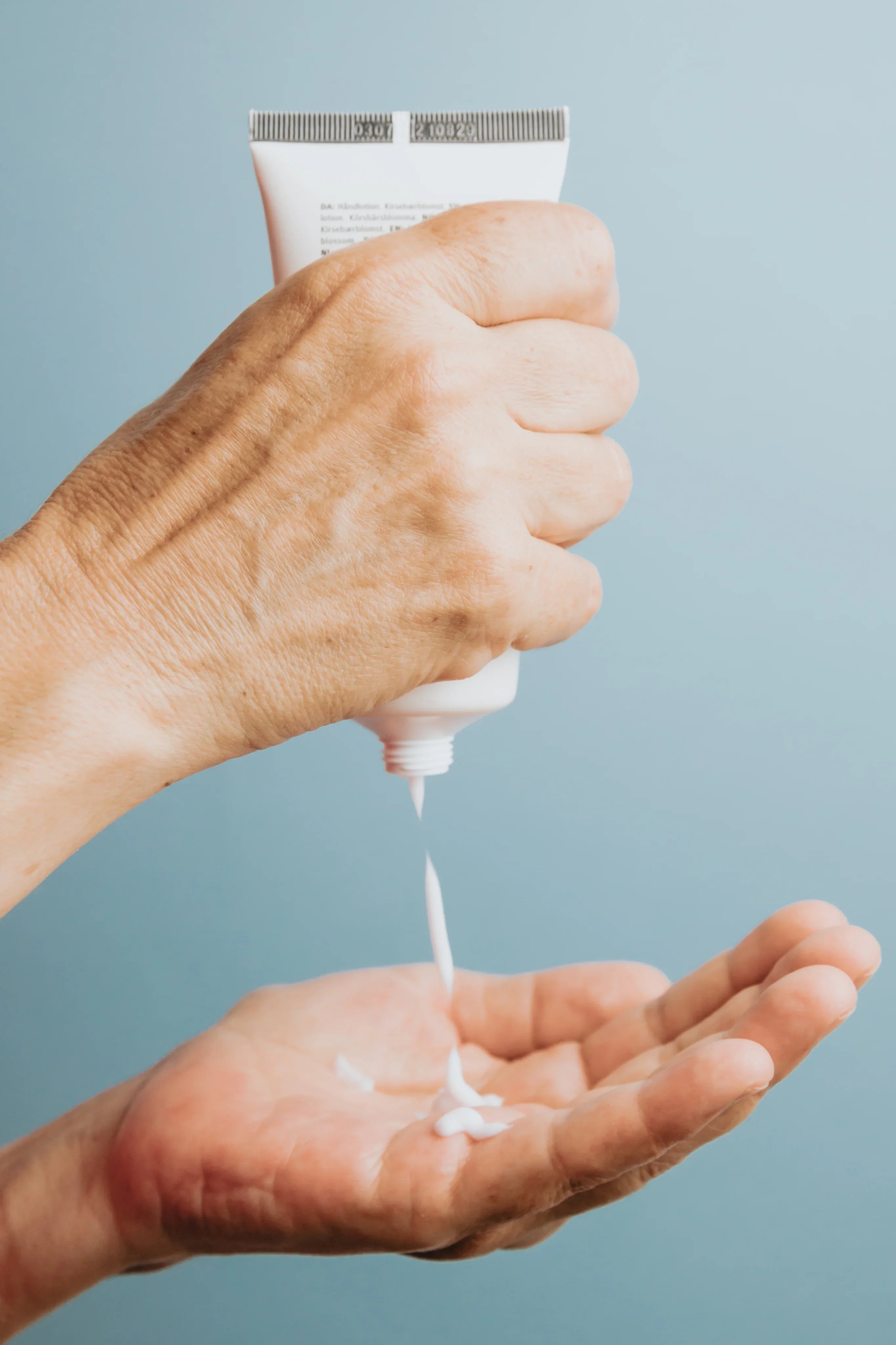 Hand squeezing white cream from tube into palm, sulfate-free skincare product